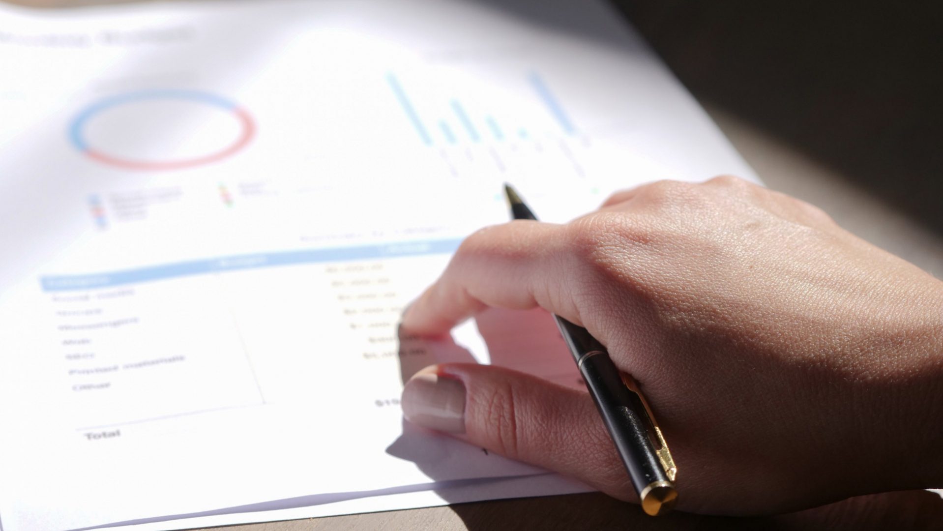 close up on hand with pen pointing to a piece of paper with charts