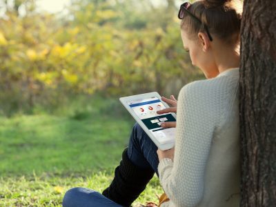 woman sitting on the grass under a tree with using an ipad to look at health plan benefit charts