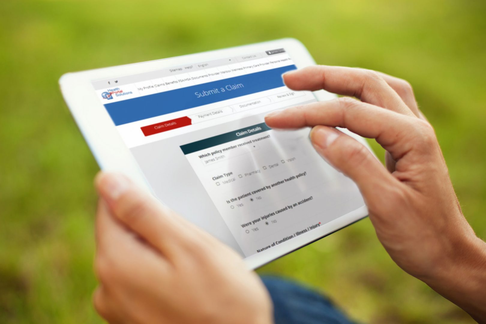 close up of hands touching an ipad to submit a claim while person is outside on the grass