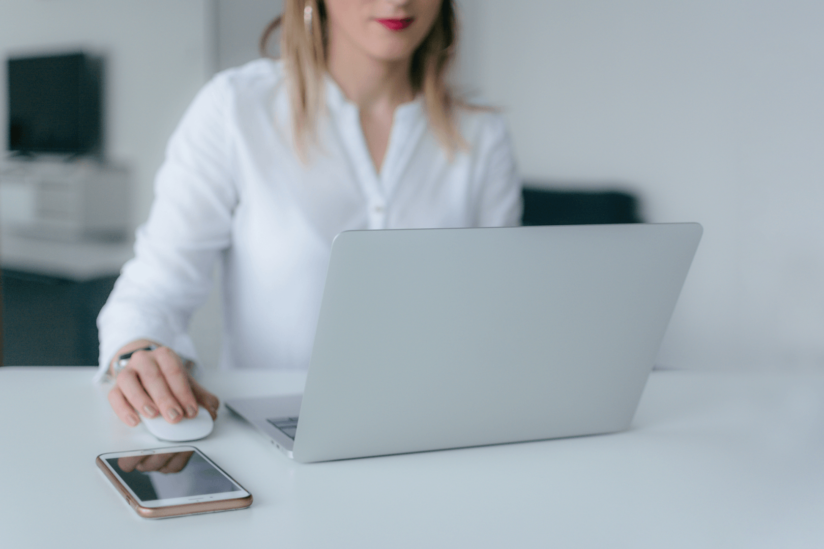 woman in a white office on a laptop using a wireless mouse