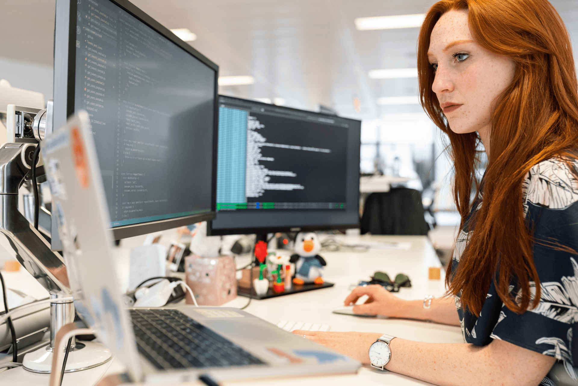 woman at a computer station with 3 screens and toys on her desk while editing code