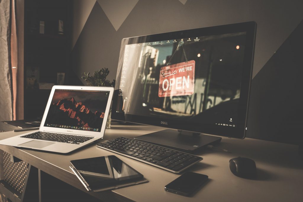 laptop and desktop with a "We're Open" sign displaying