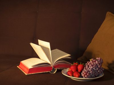 open book on a sofa next to a bowl of fruit