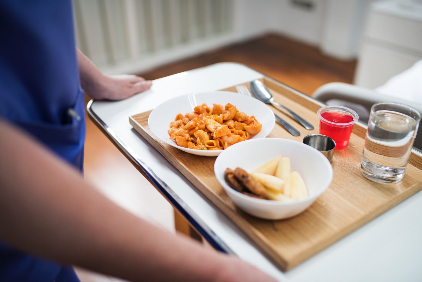 medical aid walking in a tray of food to patient room