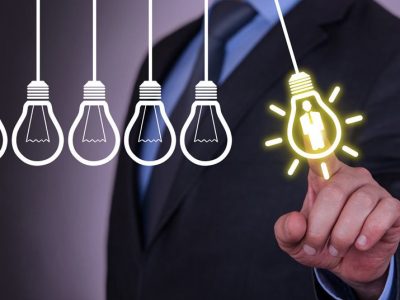 man touching a lit up lightbulb with his finger from a row of dead lightbulbs