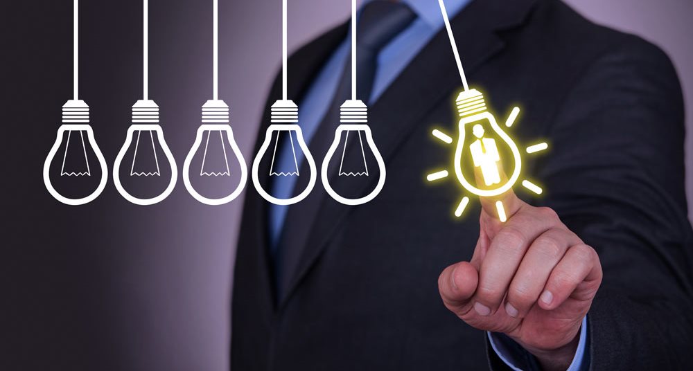 man touching a lit up lightbulb with his finger from a row of dead lightbulbs