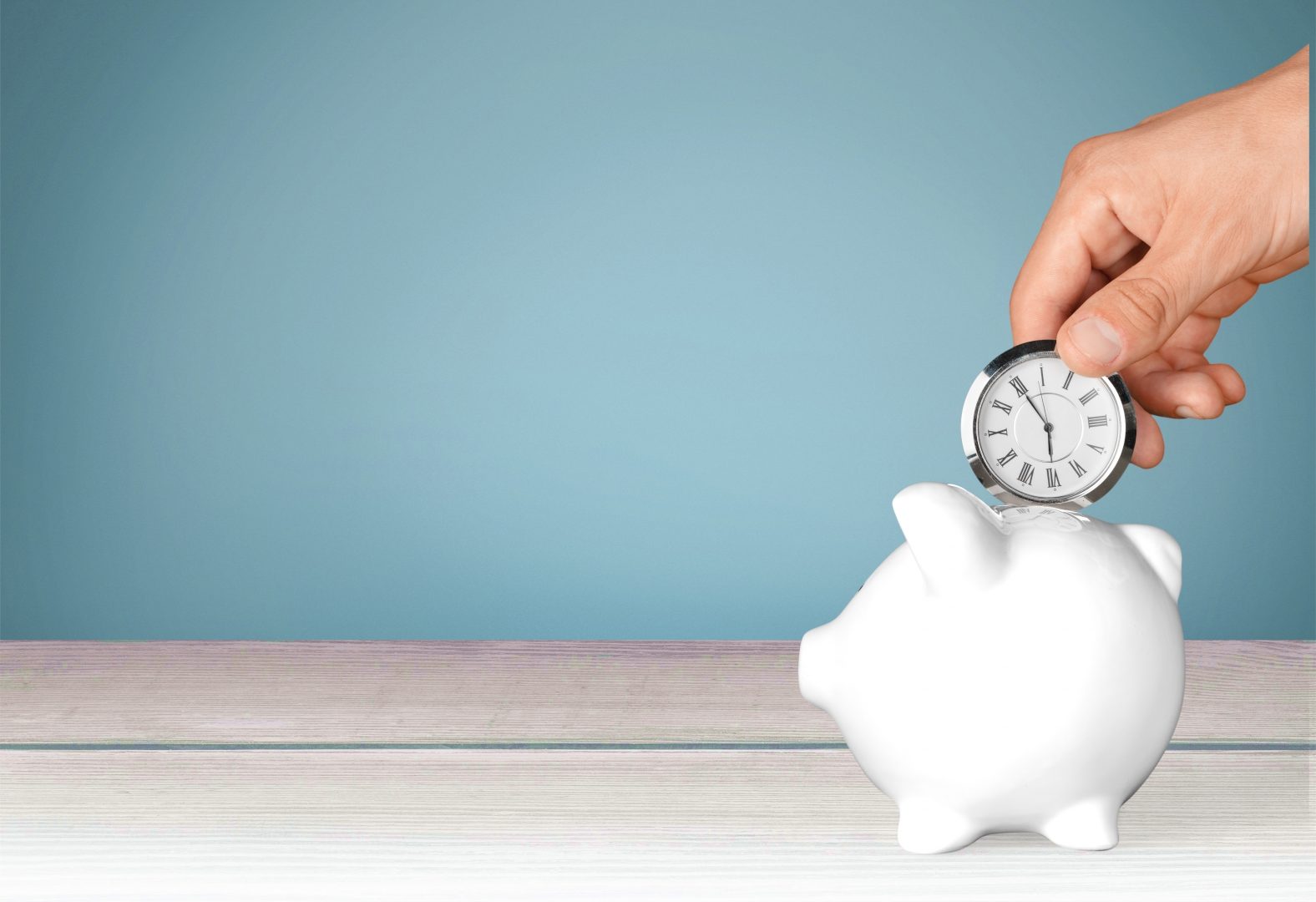 hand inserting a small clock into a piggy bank