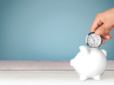 hand inserting a small clock into a piggy bank