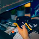 hand holding a calculator and another hand pointing at a screen with a line graph
