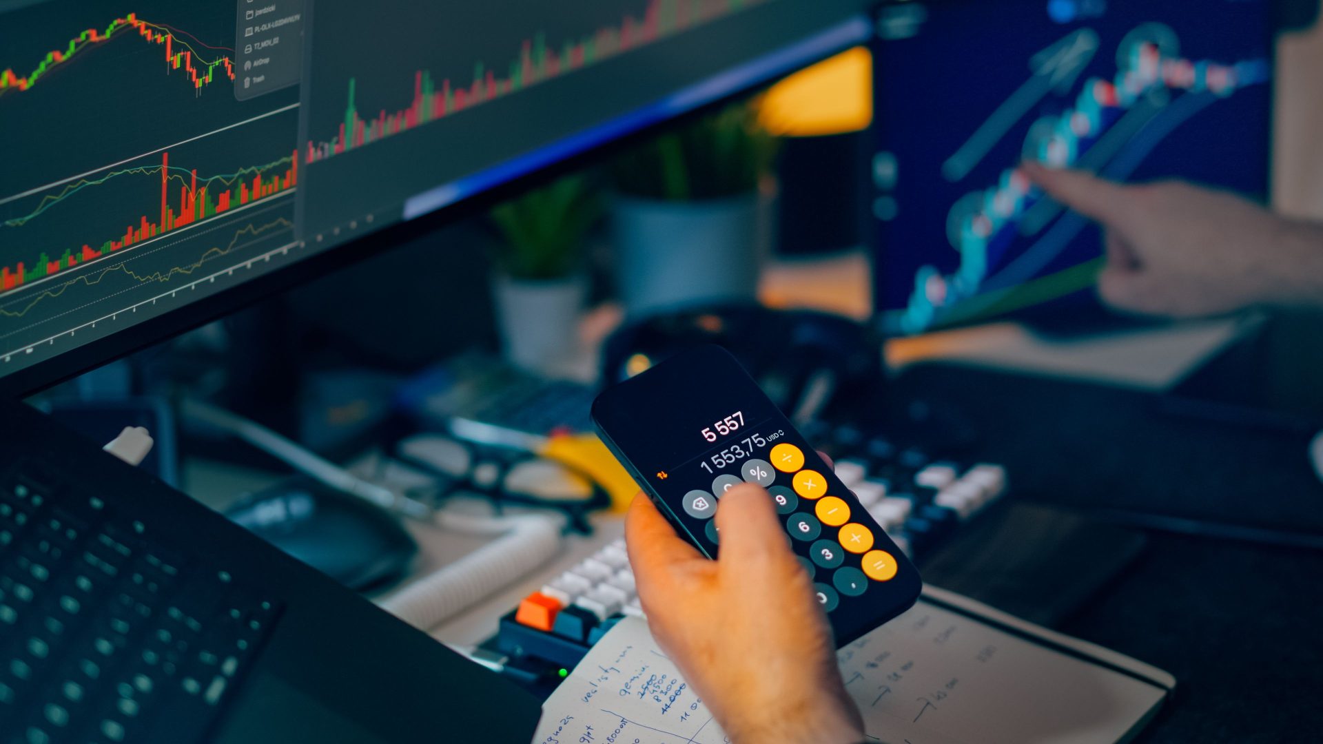 hand holding a calculator and another hand pointing at a screen with a line graph